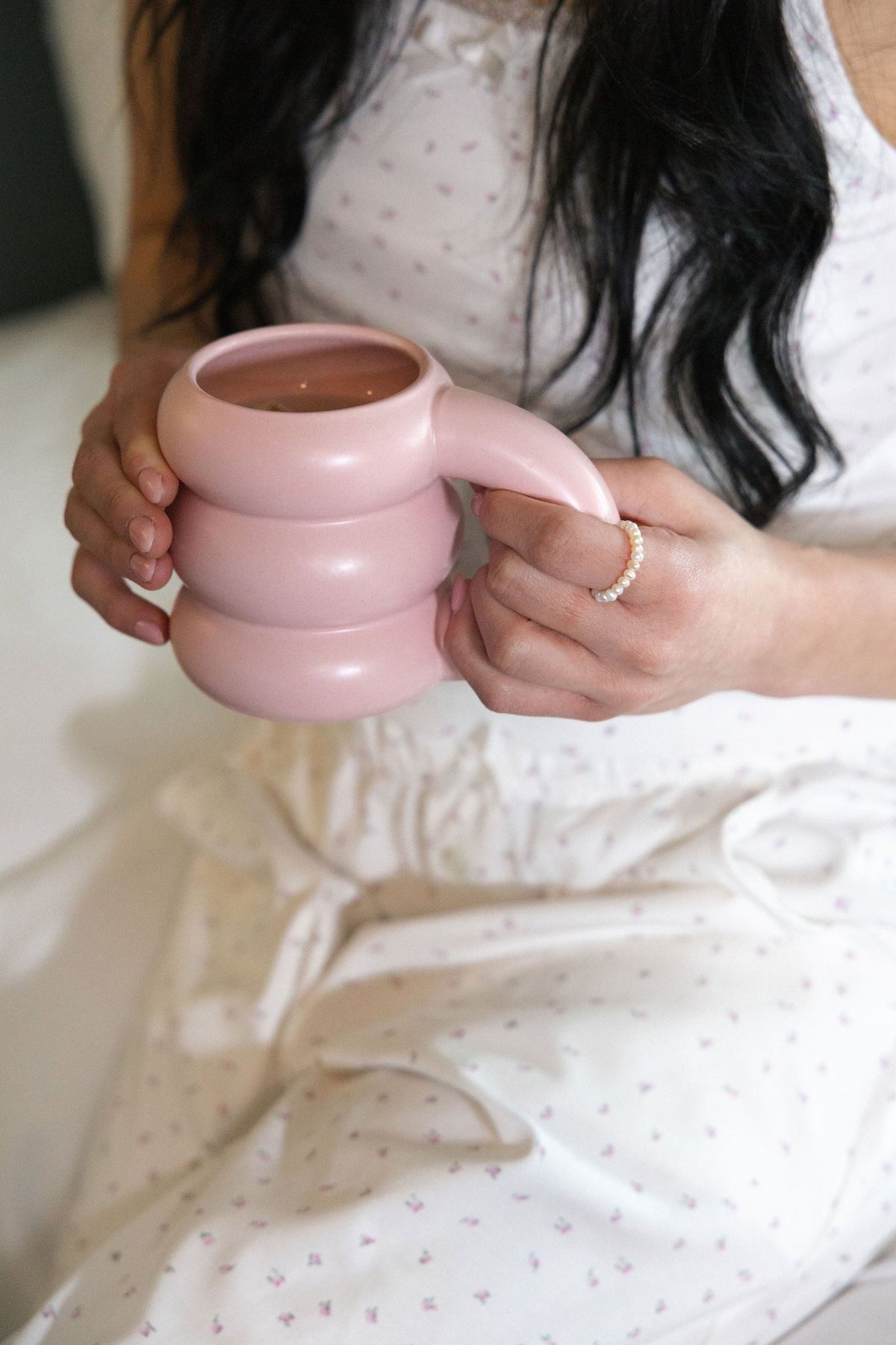 The Love Letter cotton pajama pants in Garden floral, seated and holding a pink ceramic mug