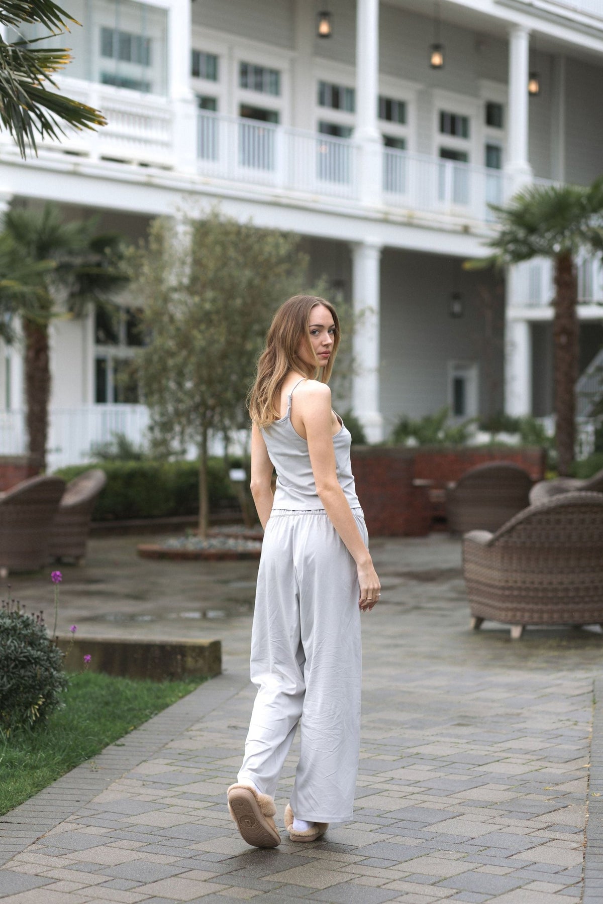 Back view of The Moonmilk cotton pajama pants in Stone, worn outdoors with slippers