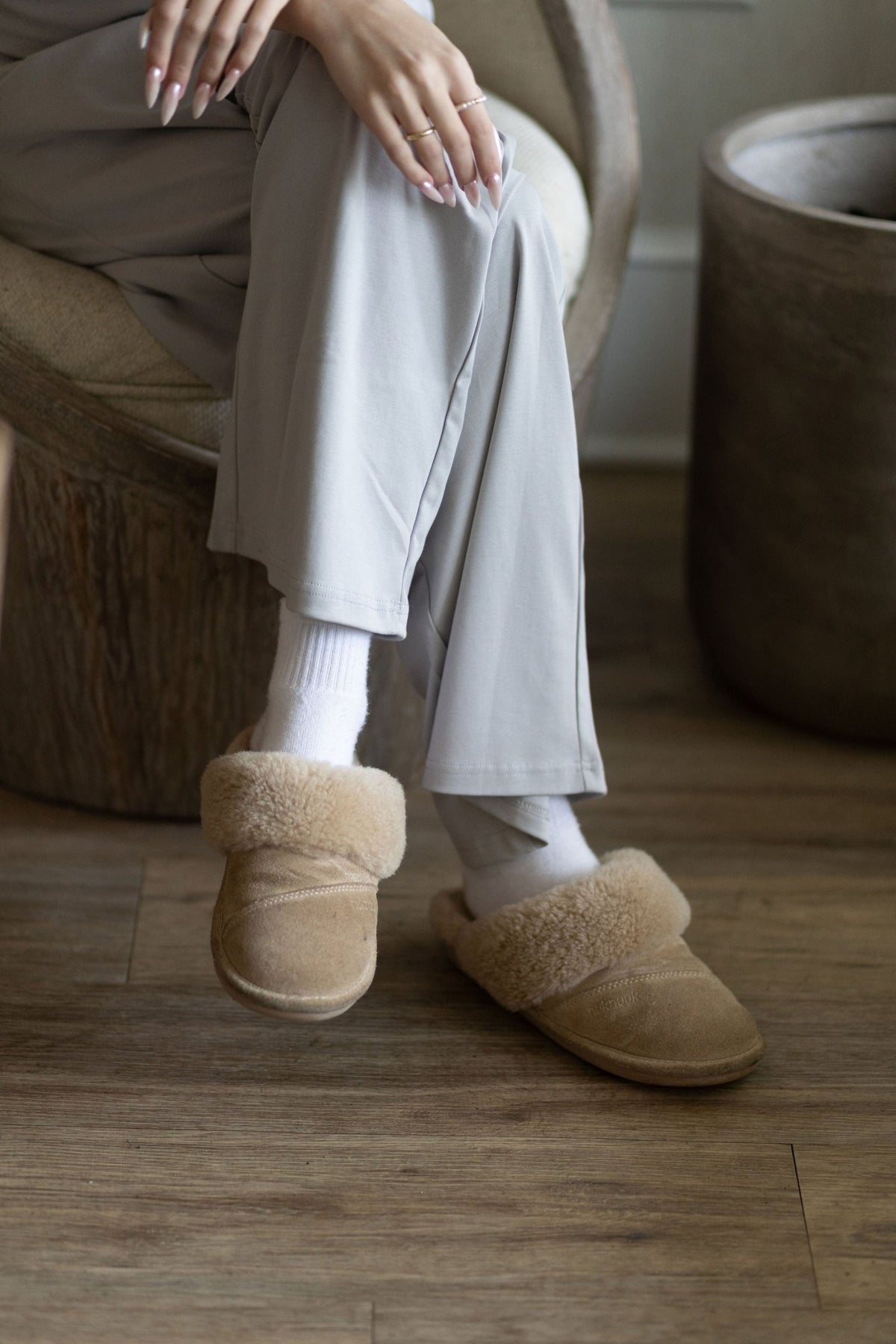 The wide leg hem of The Moonmilk cotton pajama pants in Stone, worn seated with socks and sheepskin slippers