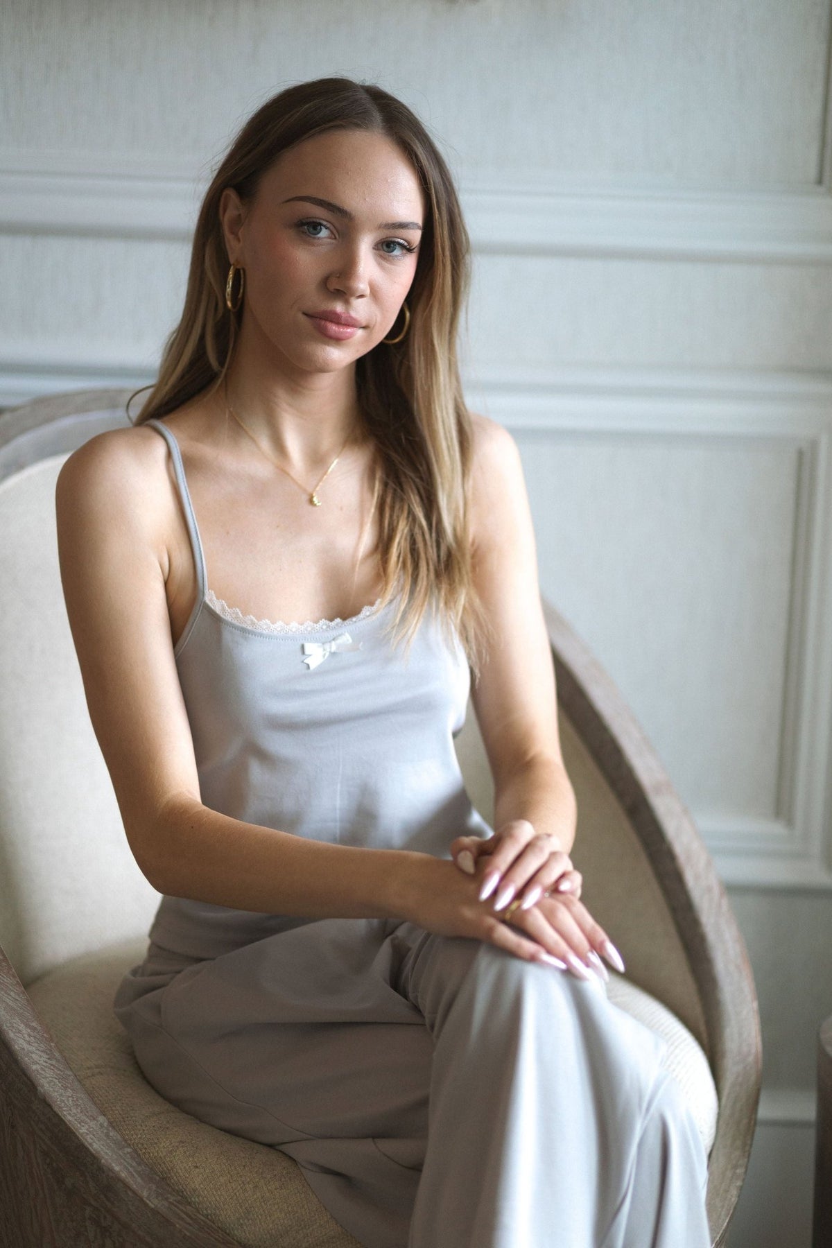 The Moonmilk cotton pajama top in Stone worn seated in a cream armchair with the matching pants
